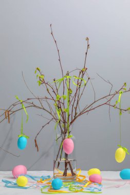 Tomurcuklu huş dalları renkli Paskalya yumurtalarıyla süslenmiş cam bir şişenin içinde. Gri arka planda ev için bir bahar kompozisyonu.