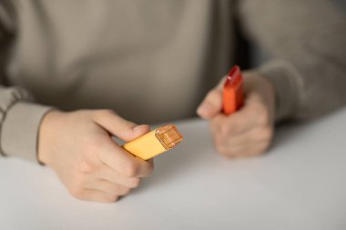 Beyaz bir masada oturan bir gencin elindeki elektronik sigaralar sağlığa zararlı ve sigara ve sigara içmekten zarar görüyor.