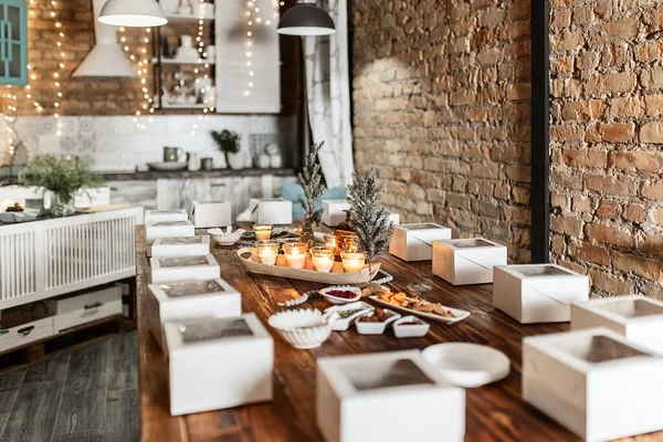 white boxes with cupcakes, cups with decor and spices on a wooden table with candles and a fir tree, preparation of a women's Christmas master class