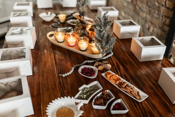 white boxes with cupcakes, cups with decor and spices on a wooden table with candles and a fir tree, preparation of a women's Christmas master class