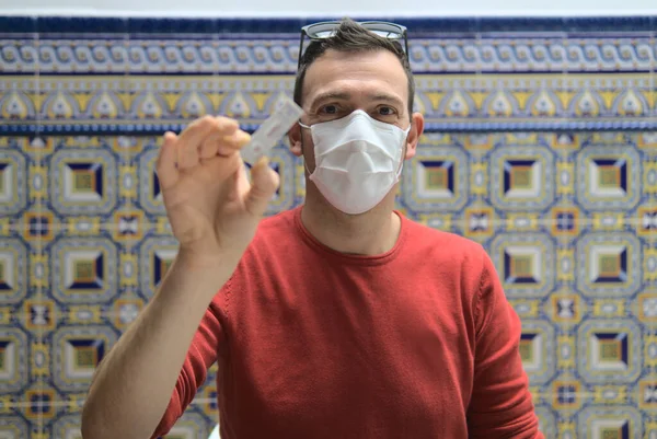 Caucasian man wear face mask and show domestic antigen rapid test with unrecognizable COVID-19 result. Tile background. Concept coronavirus