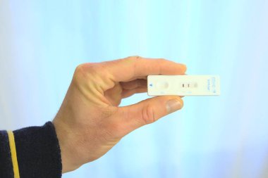 Hand of man in robe holding an antigen rapid test at home. Positive result. Concept COVID-19 desease pandemic