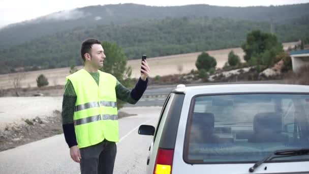 Водитель в режиме видеоконференции с центром страховой помощи. Желтый светоотражающий жилет. Аварийный маяк V16 на поврежденной крыше автомобиля. Помощь вспышки, обязательной для замены треугольников в Европе. DGT Испания — стоковое видео
