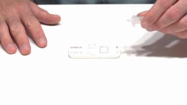 Hands of person leaving drops of liquid in a combined covid-19 and flu A+B antigen test