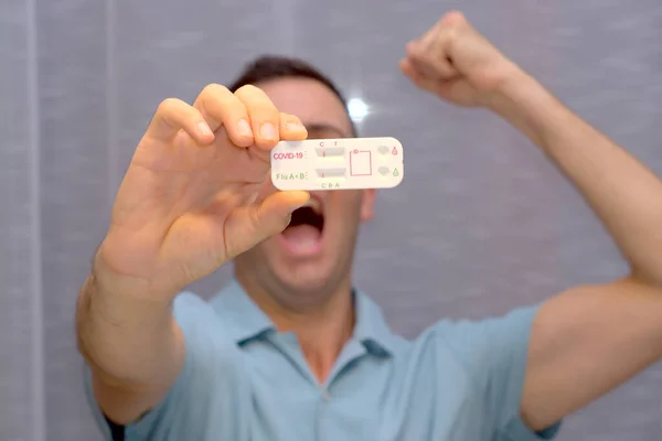 Man celebrates negative result and displays a duo rapid test for covid and flu A+B