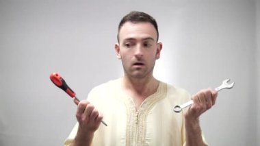 Komik Arap adam alet anahtarını ve tornavidayı kullanmakta tereddüt ediyor. Güvenilmez tamirci kavramı. Yüksek kaliteli FullHD görüntüler