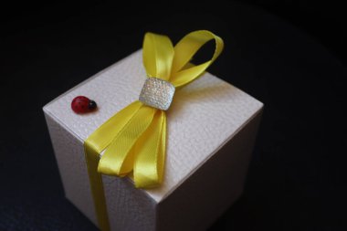 Beyaz hediye kutusu, üzerinde sarı fiyonk var.