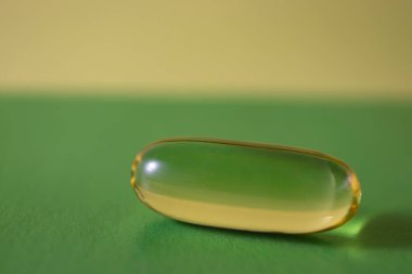 Omega 3 ve D vitamini içeren balık yağı kapsülleri. Hafif arka planda sarı kapsül. D vitamini güneş olmayınca seni sağlıklı tutar. Güneşli bir günde güneş ve mavi gökyüzüne karşı sarı vitamin kapsülü. Tedavi kavramı. 