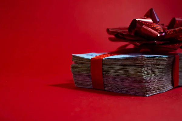 Concept, money as a gift, win or bonus. Many banknotes are tied with a red ribbon with a bow. Isolated on a red background. Christmas Bonus.