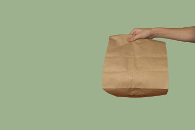 Yeşil arka planda kağıt torba. Elinde bir paket kağıt var. Ev teslimatı kavramı.