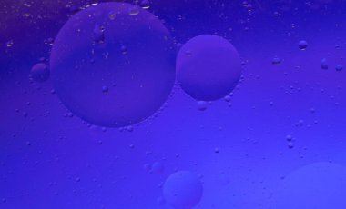 Arka planda renkli bir dokuya su damlıyor. Yağlı cam, renkli arka plan, suda kabarcıklar. Hücreler, cam üzerindeki su damlacıkları, yakın çekim makro görünümü, su hayattır, seçici odaklanma.