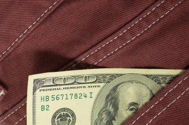 İçinde dolar banknotları olan kırmızı kot pantolon. Yıpranmış kotun ön cebinde 100 dolar ve 100 avro var. Yakın plan. Kotun cebinde 100 dolarlık banknotlar.