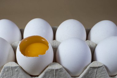 Tavuk yumurtalarının yarısı kırılmış, sabah güneşi altında yakın plan çekimde. Karton tepside tam ve kırılmış tavuk yumurtaları..