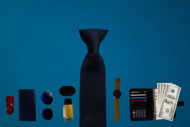 Men's Accessories. Male Items on a Blue Background Shot from Above with Glasses, Notepad, Money, Watches, Cologne, Charger and Headphones.