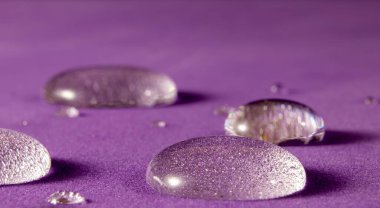 Mor Arkaplanda Su Damlacıklarının Fantastik ve Güzel Macro Fotoğrafı. Güzel Şeffaf Yağmur Damlaları, Makro, Anlaşıldı Uzay. Doğanın parlak renkli sanat görüntüsü. Doğa kavramı..