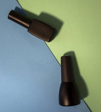 Renkli bir masa üzerinde siyah oje şişeleri. Mavi ve açık yeşil arka planda parlak ve parlak tırnak cilası şişeleri. Manikür Aletleri, Güzellik, Tırnak Sanatı Konsepti. Seçici Odaklanma. Şık Moda Kadın Manikürü.