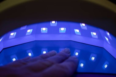 UV lambası. Ultraviyole lambadaki çivileri kurutmak. Kadınların Ellerinin Güzelliği. Arka planda ultraviyole lambasıyla oje süren kadın..