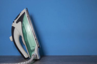 Tahta Masa 'da yeni Yeşil Demir. Demir ütü çarşafları. Mavi duvarın yanındaki çarşaf ve kıyafetlerin bakımını sağlayan modern bir cihaz. Konforlu Ev, Çamaşır ve Ütü. Boşluğu Kopyala ile Ön Görünüm.