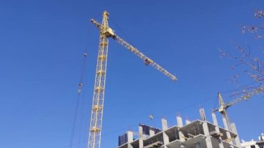 Vinçler bir apartmanın yanında. Mavi Gök ve Parlak Güneş 'in Arkasında Yapı Turnaları. Güneşli bir günde inşaat alanı. Ukrayna 'da Aileler İçin Yeni Evlerin Yapımı ve Çıkması.