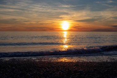 Deniz Dalgaları Sahilde Gün Batımı Manzarası. Calabria plajı, alacakaranlıkta İtalya. Altın sarısı ve pembe ışıklı canlı günbatımı, Renkli Bulutları Olmayan Güzel Açık Mavi Gökyüzü. Güzel Günbatımı.