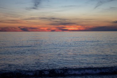 Deniz Dalgaları Sahilde Gün Batımı Manzarası. Calabria plajı, alacakaranlıkta İtalya. Altın sarısı ve pembe ışıklı canlı günbatımı, Renkli Bulutları Olmayan Güzel Açık Mavi Gökyüzü. Güzel Günbatımı.