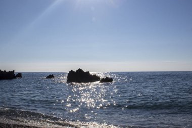 Geniş Ekran Kayalıklı, Taşlı ve Dalgalı Deniz Burnu. Deniz Dalgaları Sahildeki Kayaları Çarpıyor. Muhteşem Mavi Deniz 'in yüzeyinde Güneş ışınları oynuyor..