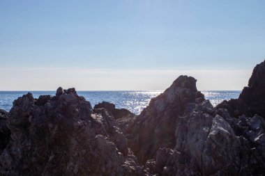 Geniş Ekran Kayalıklı, Taşlı ve Dalgalı Deniz Burnu. Deniz Dalgaları Sahildeki Kayaları Çarpıyor. Muhteşem Mavi Deniz 'in yüzeyinde Güneş ışınları oynuyor..