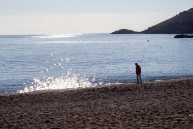 Scalea, İtalya 12 Nisan 2022: Kayalık bir kıyıda bir çocuk açık bir günde öğleden sonra mavi denize bir taş atıyor. Deniz kenarındaki çocuk. Mutlu çocukluk.