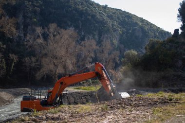 Kazı Kazıcı. İtalya, Calabria 'daki Dağların Arkaplanı' na karşı nehir kıyısındaki inşaat alanı. Kazıcı, Kazıcı, Kazıcı.