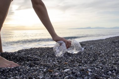Adam plajı plastik şişelerle ve turistlerin arkasından deniz kıyısındaki çöplerle temizliyor. Gönüllü Kavram. Çevre kirliliği. Ekolojik sorun.