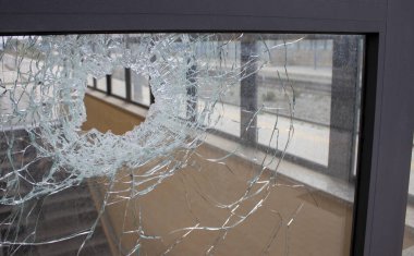 Broken Facade Window Glass. A hole in the window glass from a bullet fired during the fighting. cracks around the hole. Dirty Window Frame. View of the street from the inside.