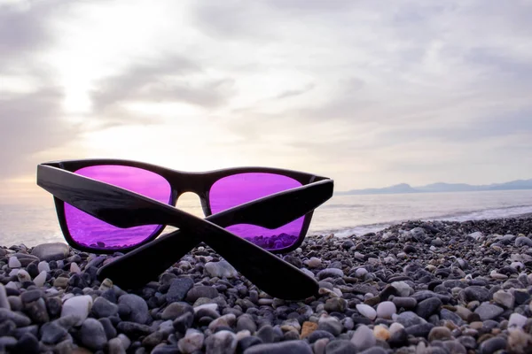 Evening Tropical Beach Vacation, Sunset Sunglasses. Sunglasses Lying on Tropical Stony Clean Beach. Sunglasses on the Beach. Beautiful Sea View Wallpaper Background.