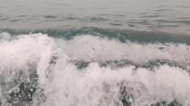 Denizde dalgaların yavaş hareketi. Yavaş hareket eden dalgalar kıyıya doğru koşuyor. Dalgalar hareket ettikçe, beyaz deniz köpüğünün dokusunu oluştururlar. Calabria Sahili, İtalya.