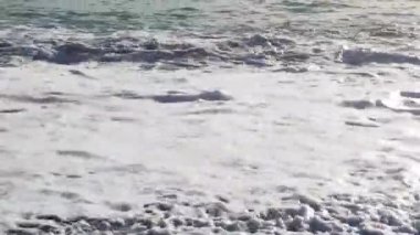 Denizde dalgaların yavaş hareketi. Yavaş hareket eden dalgalar kıyıya doğru koşuyor. Dalgalar hareket ettikçe, beyaz deniz köpüğünün dokusunu oluştururlar. Calabria Sahili, İtalya.