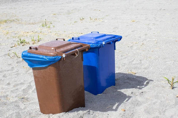 Multicolored trash cans with paper, plastic, glass and organic waste suitable for recycling. Separate waste collection, waste sorting, waste management. Natural outdoor background. Separate garbage collection. Colored trash cans. Metal, paper and pla