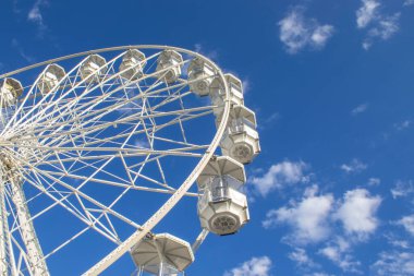 Mavi gökyüzü ve bulutlarla dolu eğlence parkı. İtalya 'da bir lunaparkta beyaz dönme dolap. Gün boyunca mavi bir gökyüzüne karşı dev bir tekerlek..