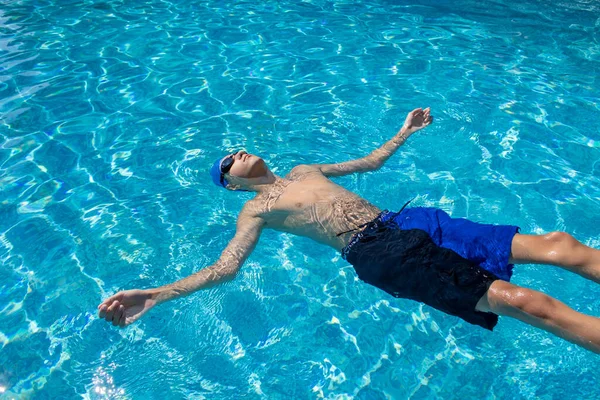 Relaxing Guy Lies in the Pool. High Angle View of a Young Man in Glasses Swimming in the Pool. View From Above.