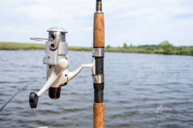 Close-up of a Fishing rod Wheel Against the Backdrop of a Fantastic Lake with Perch, Carp and Pike. Fishing on the Lake in the Morning at Sunrise or in the Evening at Sunset. Fishing Background.