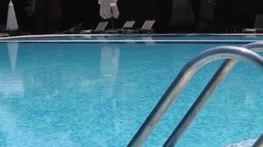 Metal Handrails by the Pool. Blue and Shining Water in the Pool Against the Backdrop of Tropical Trees, Palms, Flowers, Sun Loungers. Calm Peaceful Environment. Summer Background.