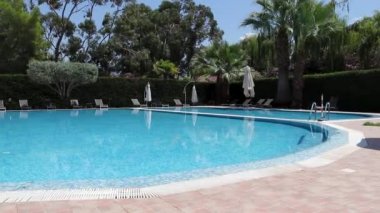 Blue and Shining Water in the Pool Against the Backdrop of Tropical Trees, Palm Trees, Flowers, Sun Loungers. Calm Peaceful Environment. Summer Background. Vacation Concept. Good Place to Relax With the Whole Family.