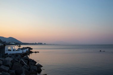Panoramic shot from the shore of the cute city of Salerno on the sea and mountains with sunrise in the background. Sunrise in Southern Italy, in Calabria. Scenic travel destination.