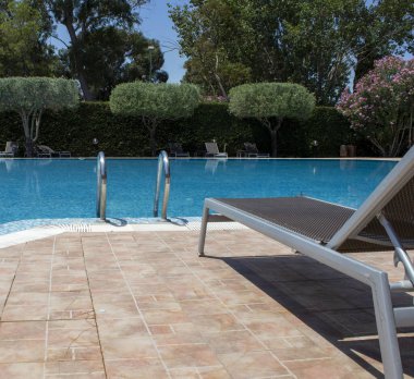 Swimming Pool in a Beautiful Garden. Gorgeous Summer Landscape in a Blue Lagoon Park Surrounded by Lush Green Trees, Grass and Plants with Blue Skies in Calabria, Italy.