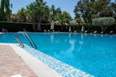 Swimming Pool in a Beautiful Garden. Gorgeous Summer Landscape in a Blue Lagoon Park Surrounded by Lush Green Trees, Grass and Plants with Blue Skies in Calabria, Italy.