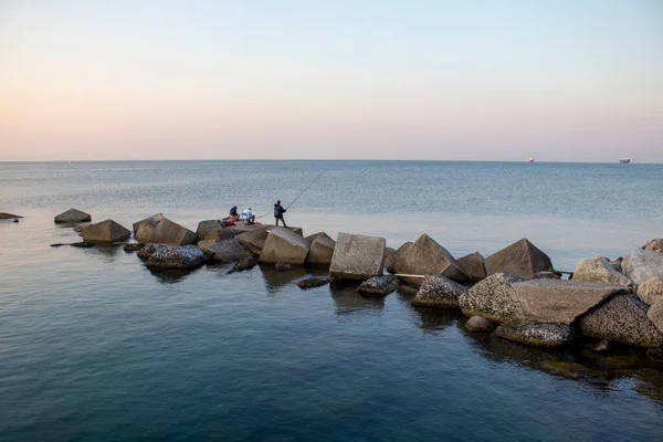 Three men are fishing on the ocean. Fishing during the holidays. Deep blue water, pleasant sky, dawn. Peaceful surroundings. Fishing as a holiday and hobby.