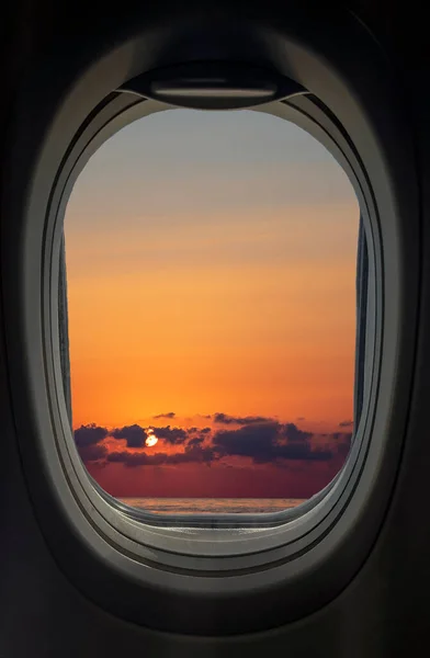 The window of the plane with a view of the sunset with fantastic clouds.