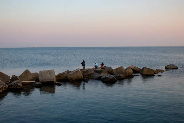 Three men are fishing on the ocean. Fishing during the holidays. Deep blue water, pleasant sky, dawn. Peaceful surroundings. Fishing as a holiday and hobby.