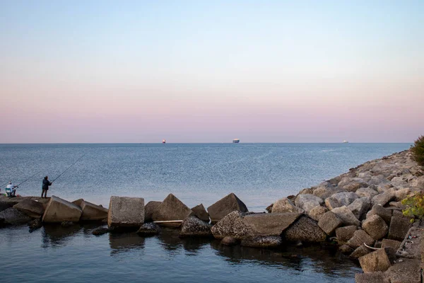 Men fish on the ocean. Fishing during the holidays. Deep blue water, pleasant sky, dawn. Peaceful surroundings. Fishing as a holiday and hobby.