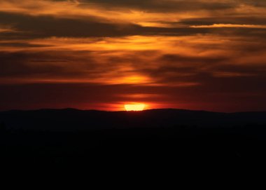 Güneşin turuncu bulutlarda ve yerin siluetinde dramatik bir gün batımı.