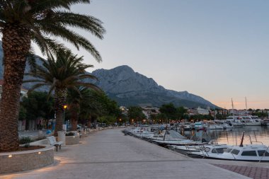Hırvatistan 'ın turistik tatil beldesi Baska Voda' daki marinada yaz şafağında boş gezinti güvertesi ve demirli botlar