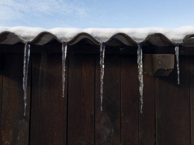 Buz saçaklarından sarkan buz saçakları, tahta binalar ve asbest çatı panelleri